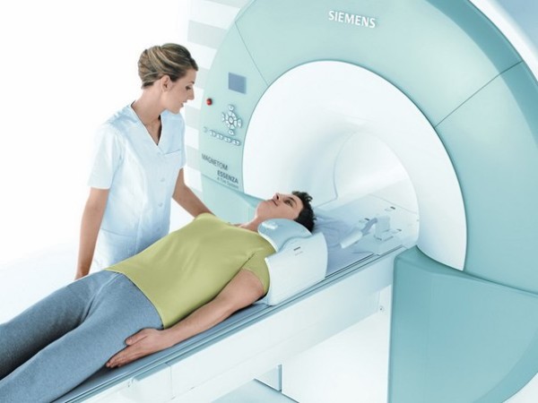 Специалист подготавливает пациента к МРТ, который лежит на подвижном столе перед отверстием сканирующего блока томографа