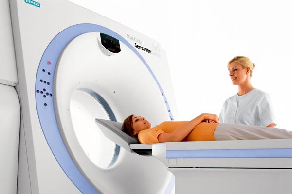 Специалист подготавливает пациента к МРТ, который лежит на подвижном столе перед отверстием сканирующего блока томографа