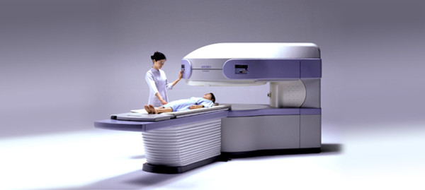 Специалист подготавливает пациента, лежащего на столе томографа открытого типа